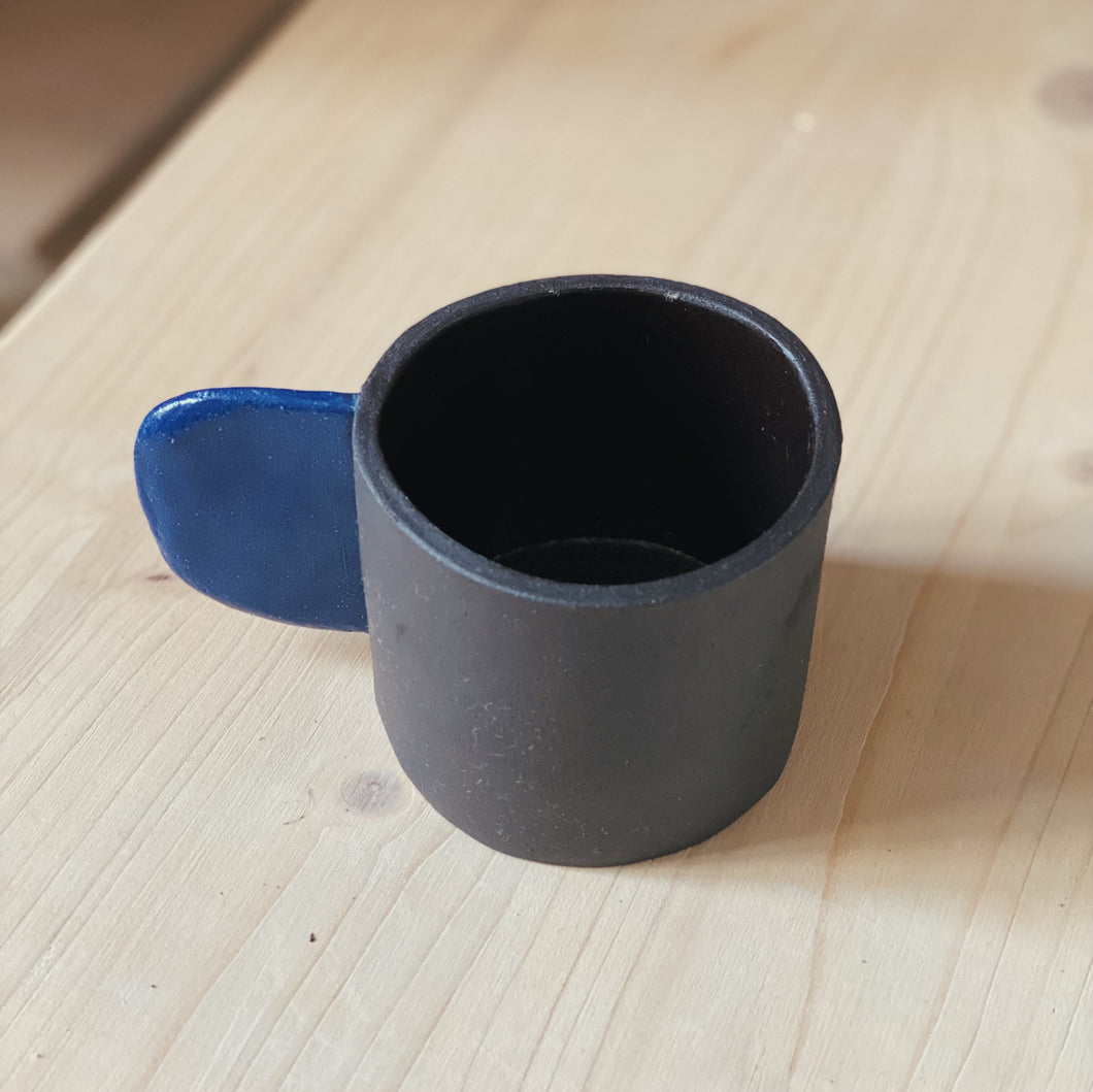 Kleine Tasse schwarz mit blauem Henkel