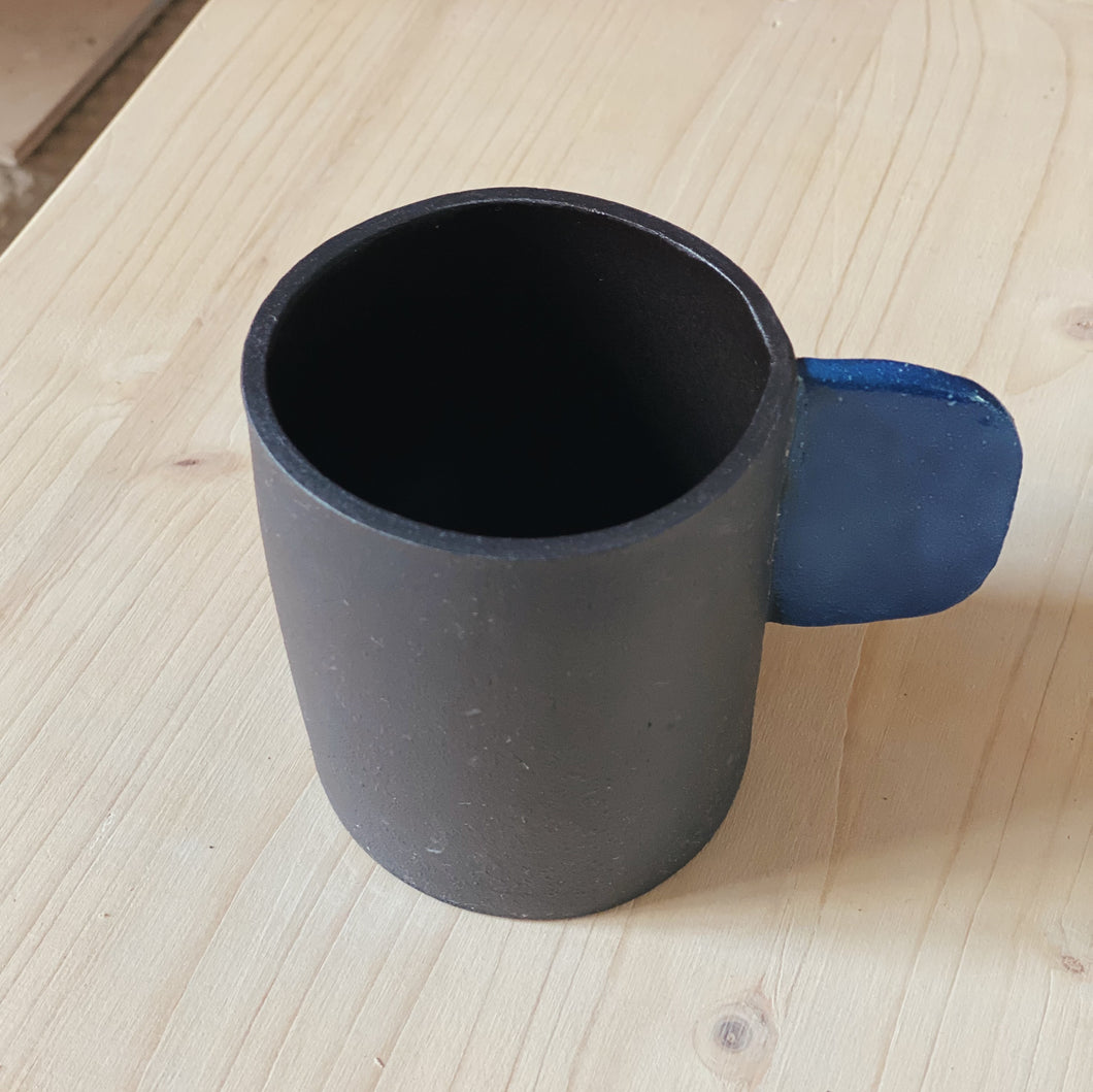 Tasse schwarz mit blauem Henkel